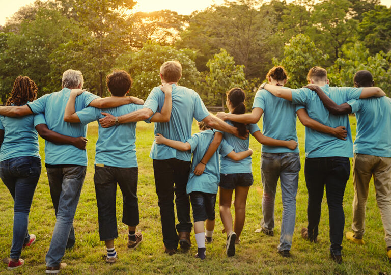 Group of people in a community with arms entwined behind back, walking in field