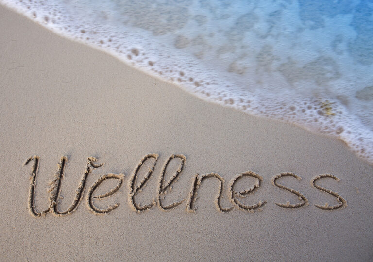 Word wellness written on the sand of the beach. Beach and wave background.